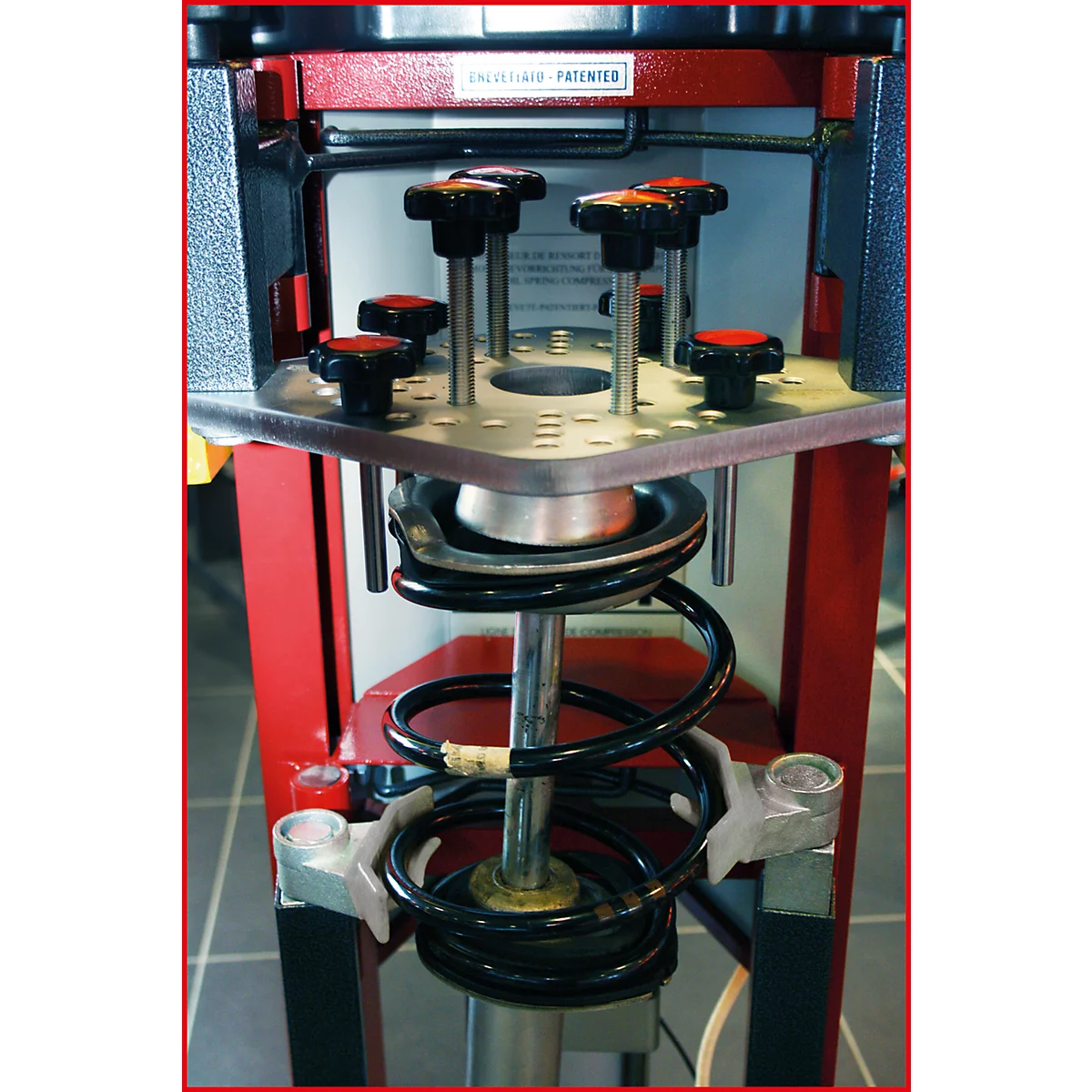 Detailaufnahme eines Federbeinwerkzeugs. Roter Rahmen, Metallkonstruktion, schwarze Feder, Knöpfe mit roten Spitzen.